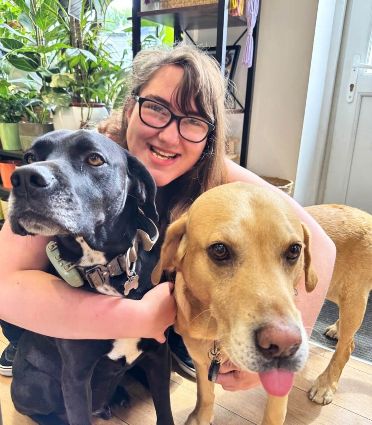 Jemma smiling with two dogs, black and golden, in a cosy indoor setting.